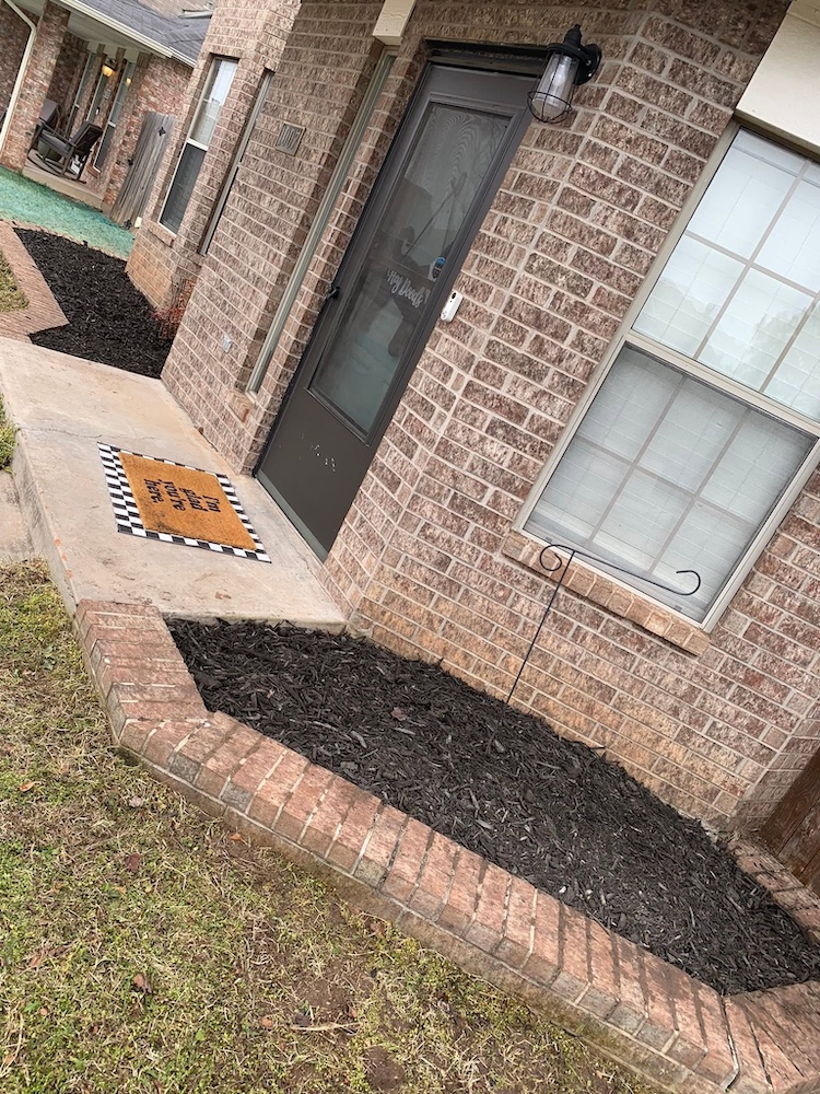 After — New mulched garden bed with clean edging along the brick wall